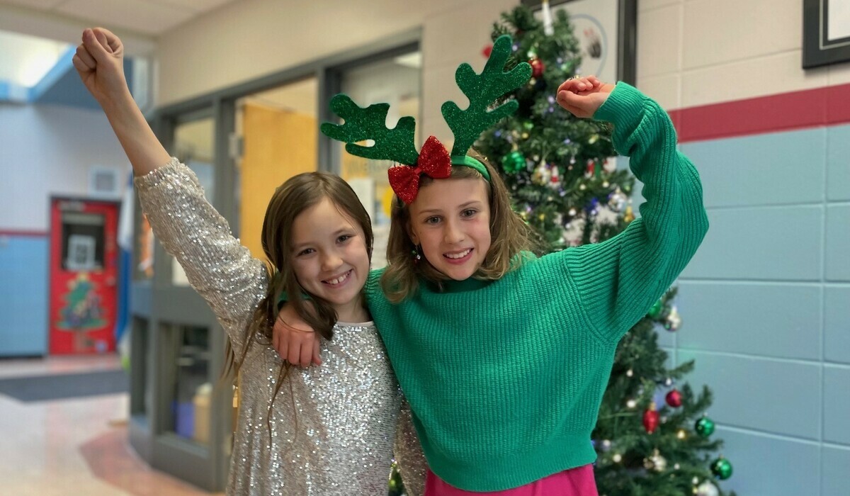 2 grade 5 students standing in front of Christmas tree with their arms in the air cheering